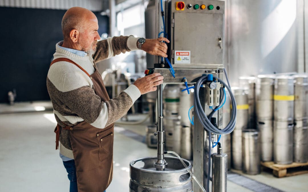 Field technician reviewing a pneumatic manipulator’s joints, air lines, and end-of-arm tooling at a manufacturing workstation during a planned service assessment.