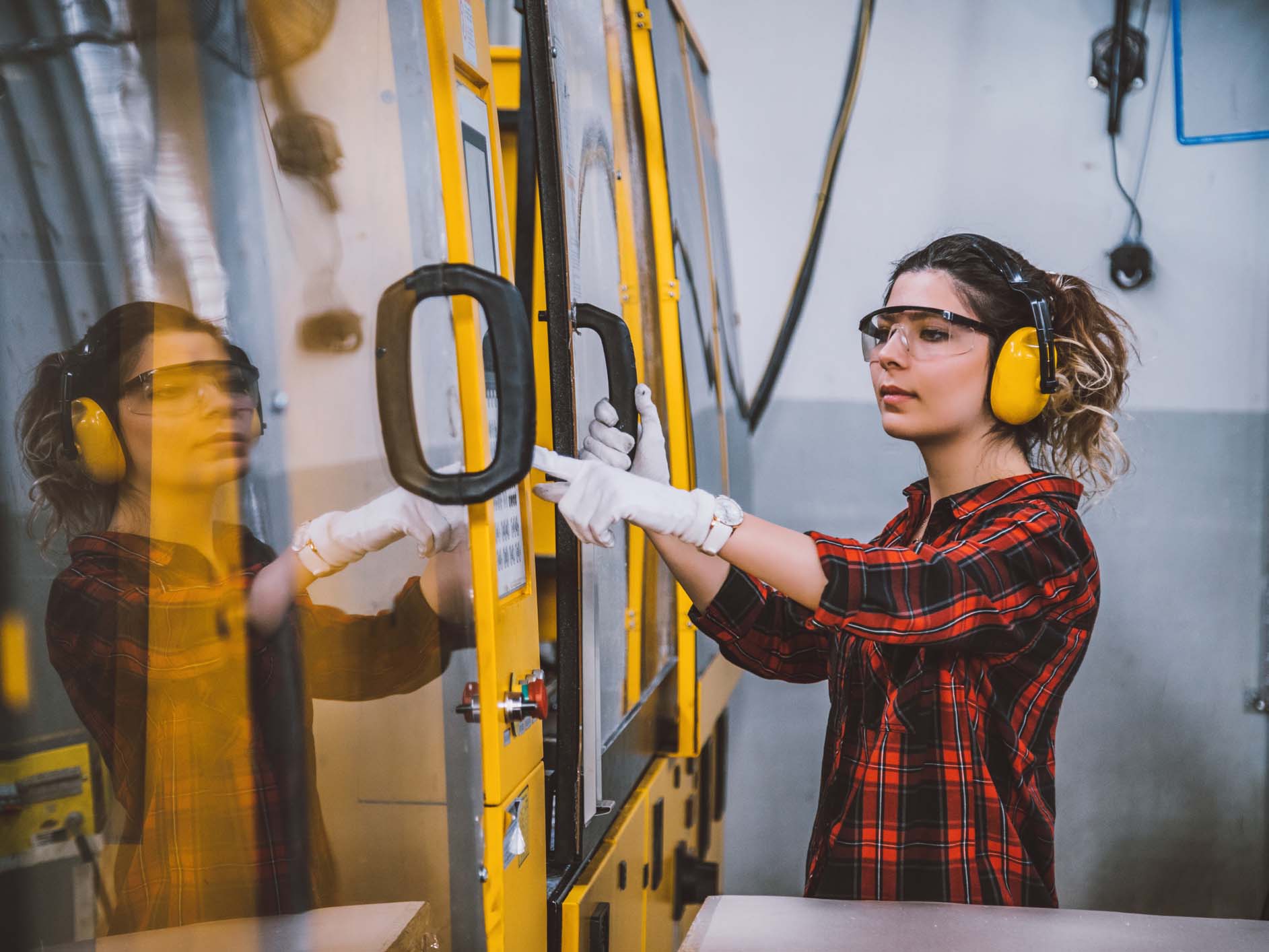 Mid-market manufacturing operator using a pneumatic manipulator zero-gravity lifting system to position a heavy component without manual strain, demonstrating ergonomic material handling equipment in action